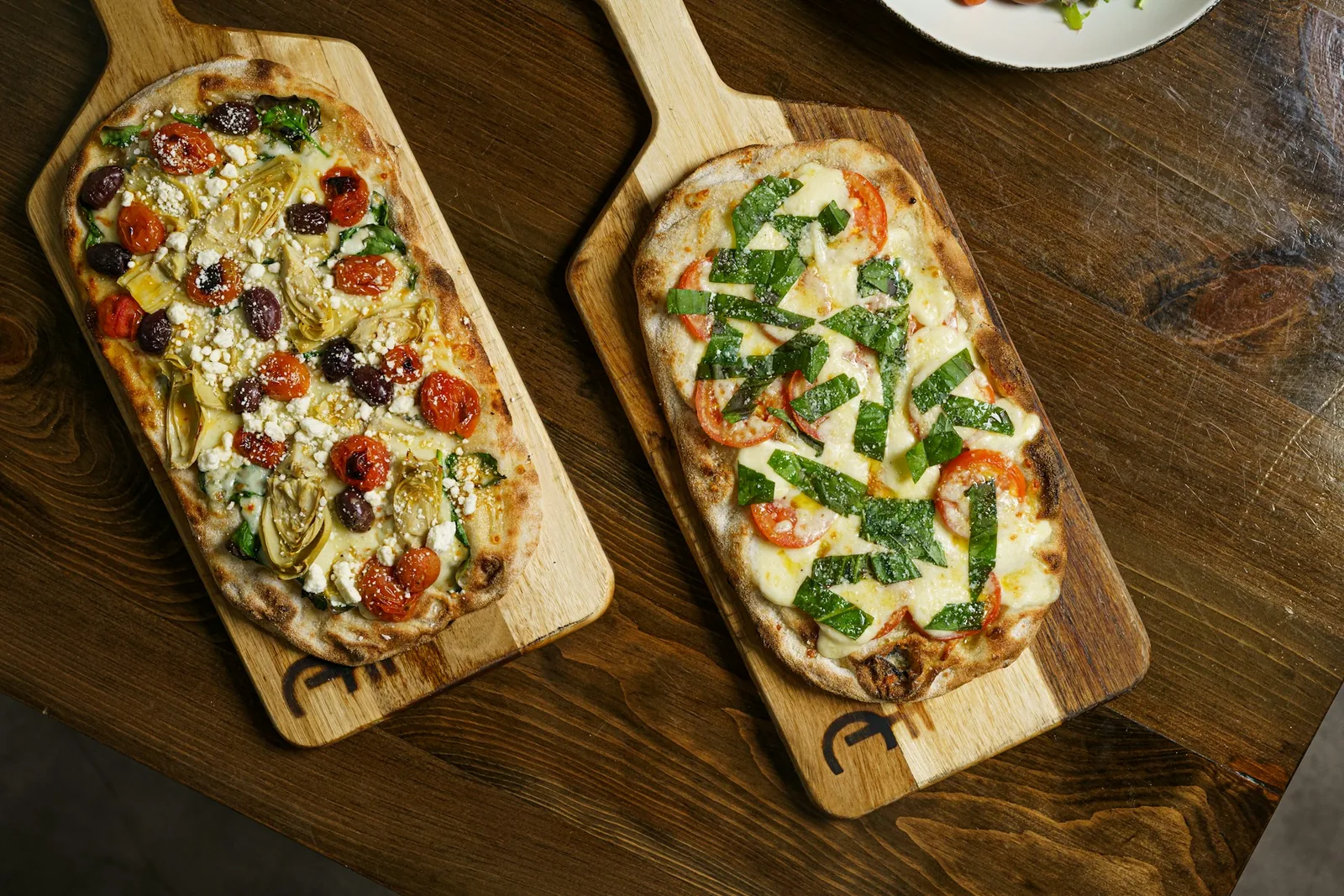 Two whole pizzas on wooden boards