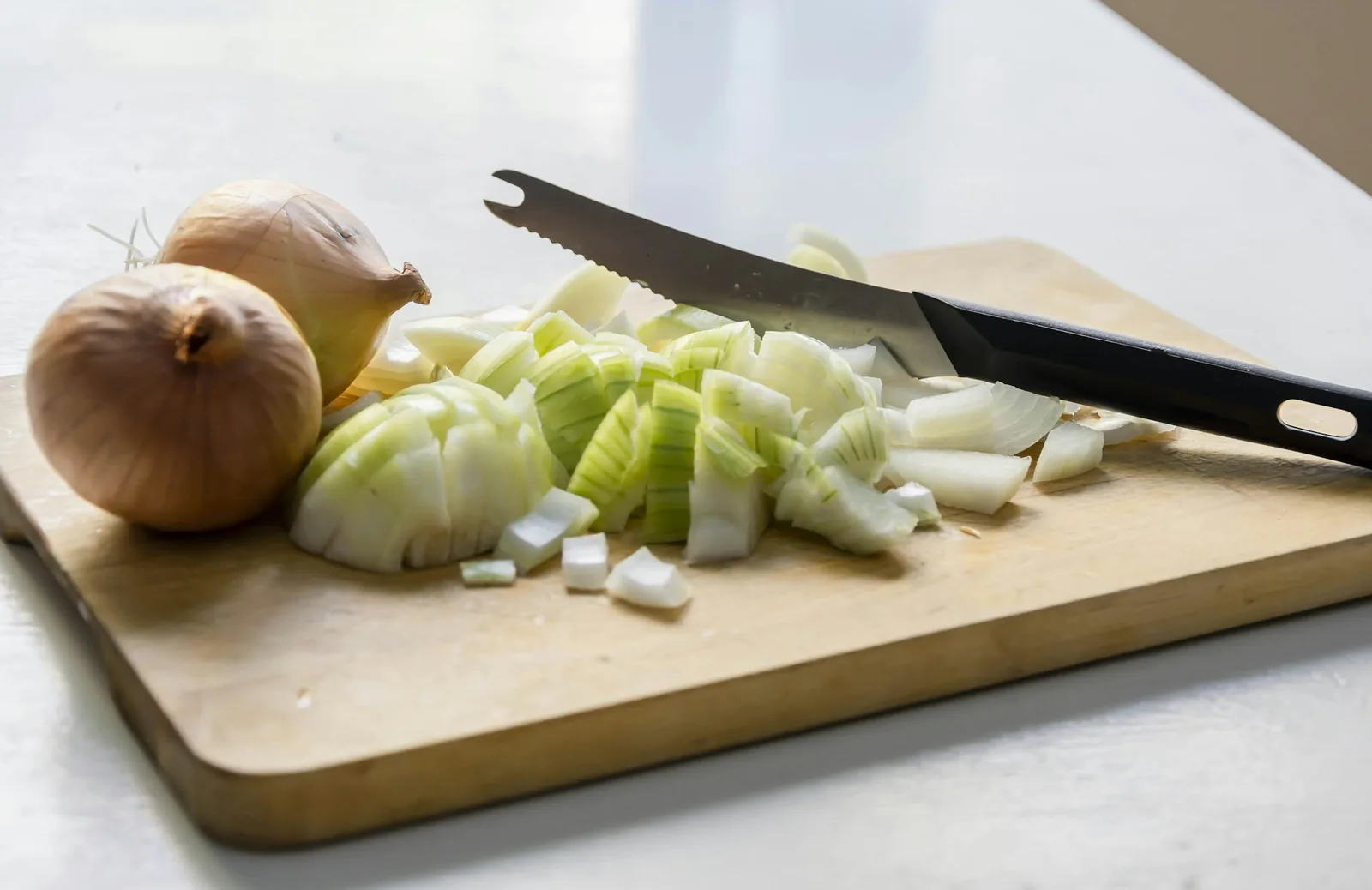 Chopped onions on a board beside a knife