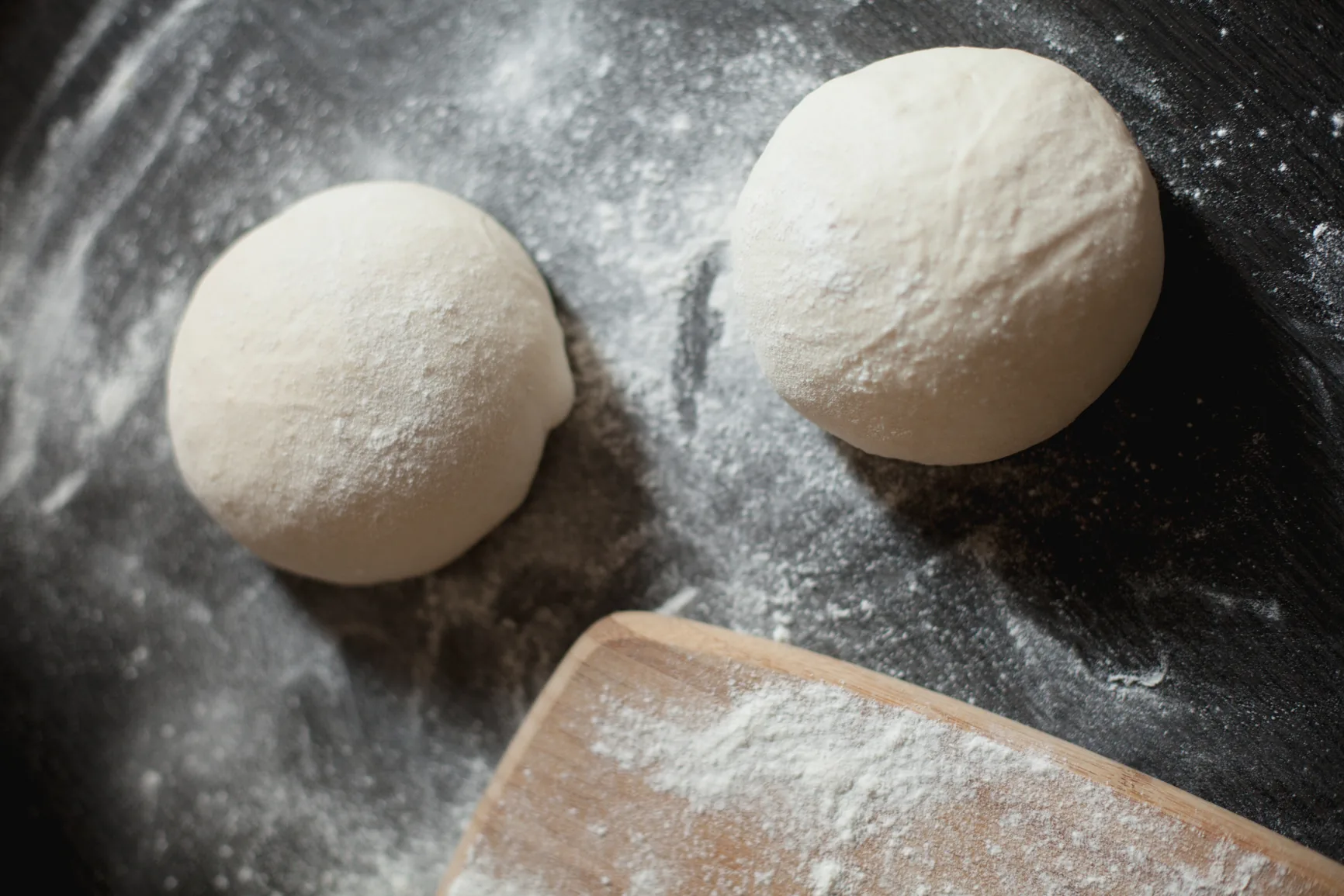 Balls of fresh pizza dough resting on a floured surface