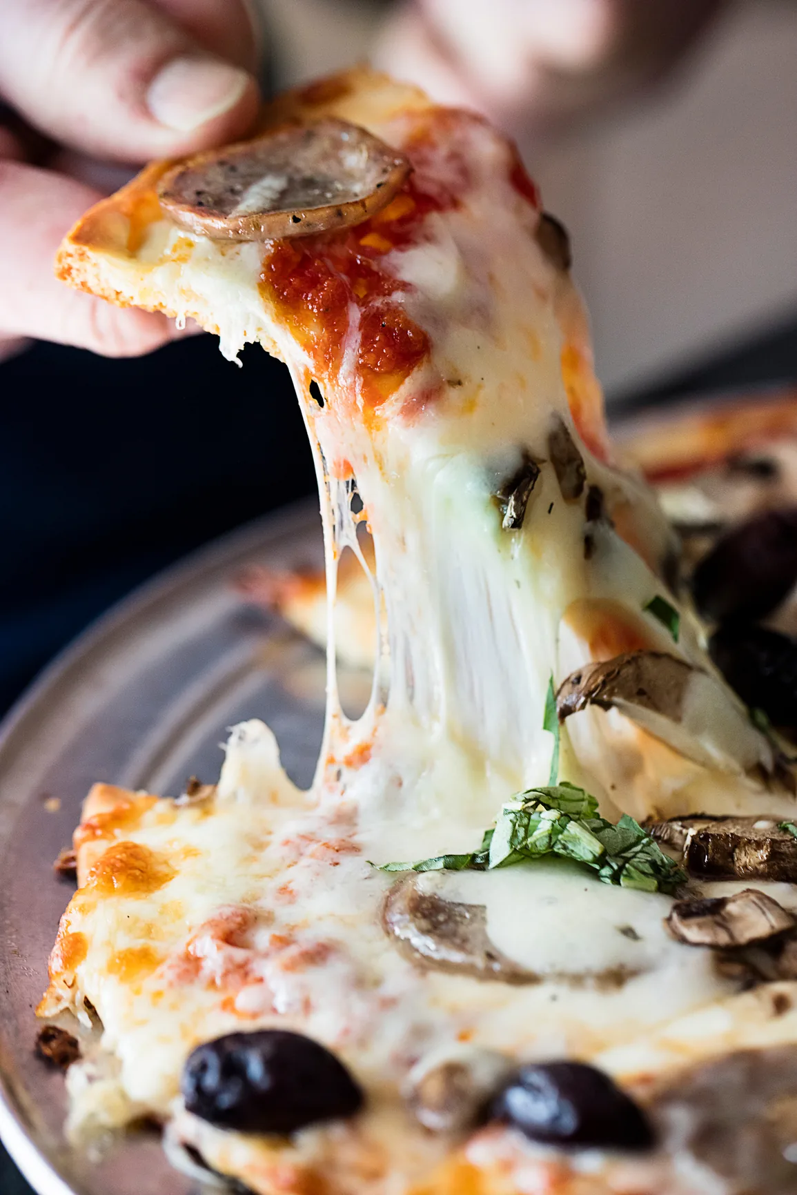 A slice of sausage, olive and mushroom pizza being lifted from the pie