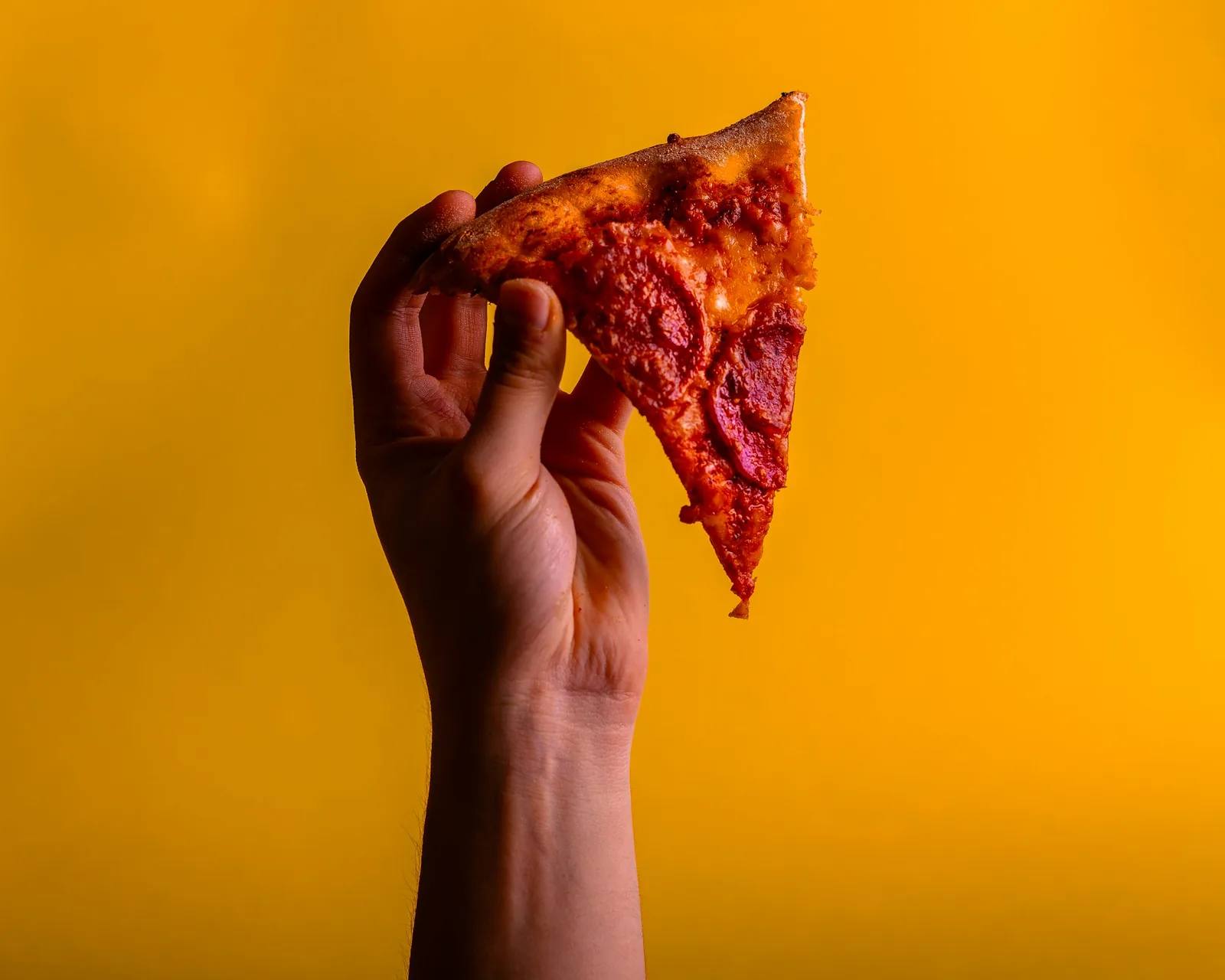 A pizza slice held against a plain background